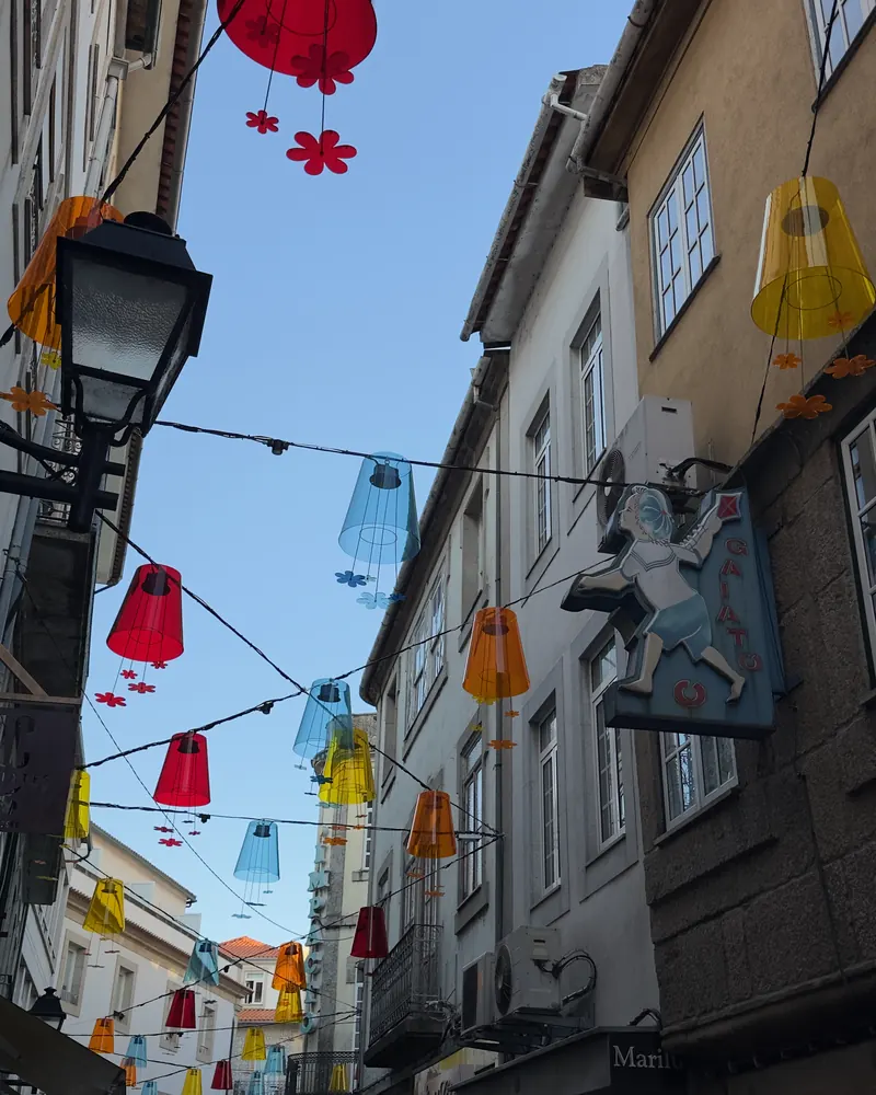 Rua estreita do centro histórico de Viseu com lanternas coloridas penduradas entre as fachadas