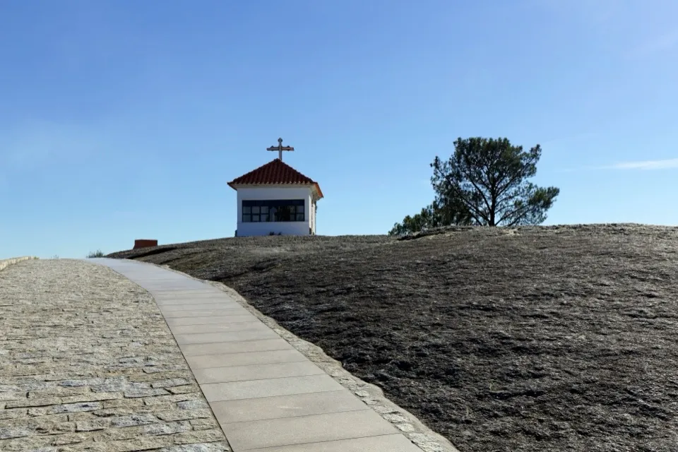 A capela branca de telhado vermelho no topo da laje de granito, com um caminho de pedra e um pinheiro, no Monte de Santa Eufémia
