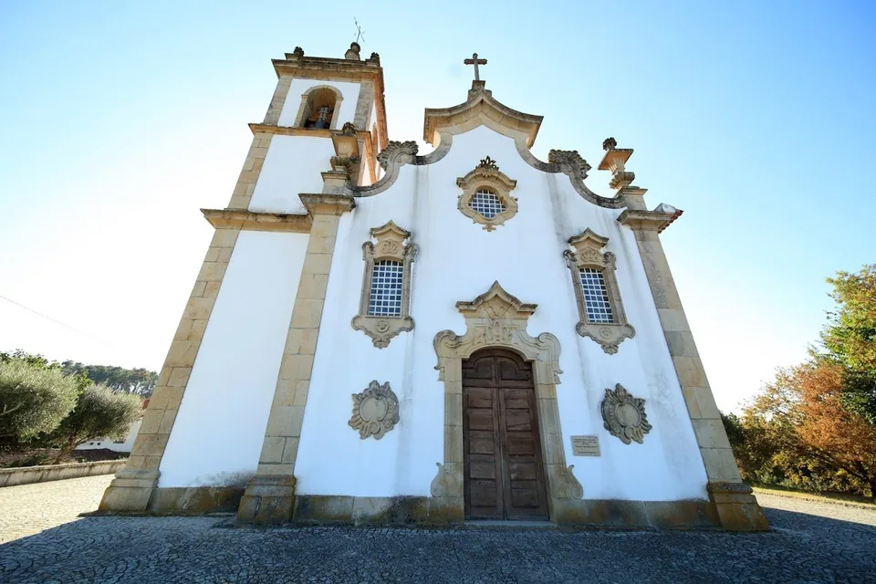Fachada branca da igreja matriz de Ribafeita, com portal de pedra, torre sineira e adro de calçada