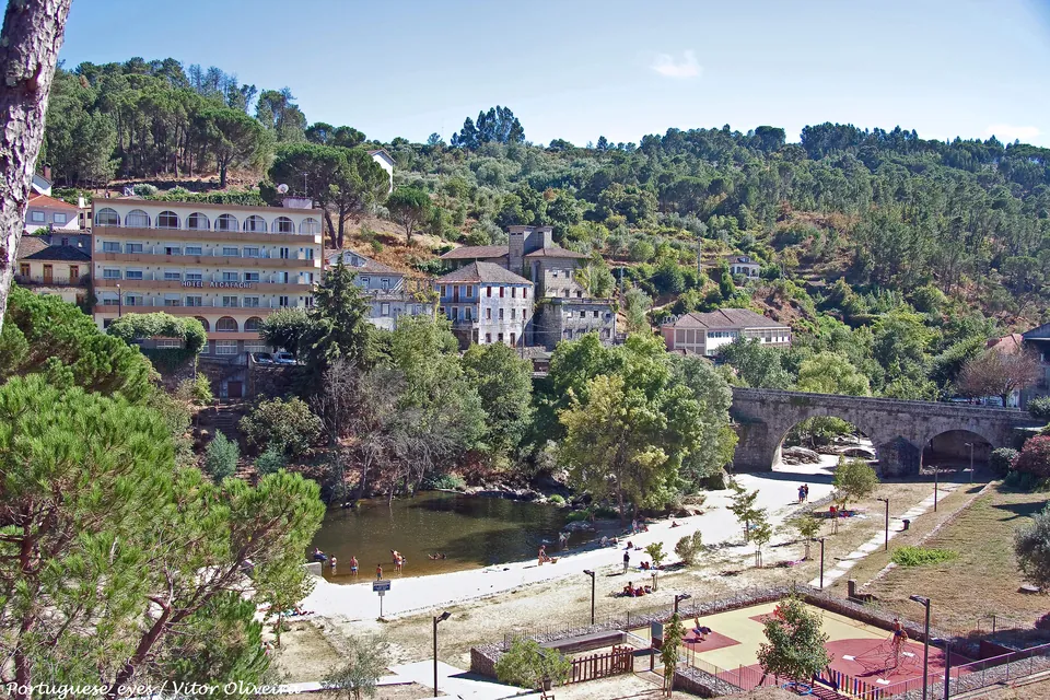 A praia fluvial do Banho no rio Dão, com a ponte de pedra e a estância termal na encosta