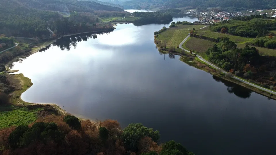 O espelho de água do rio Dão em Vila Corça, com vinhas, a estrada e a aldeia na margem, na freguesia de Povolide